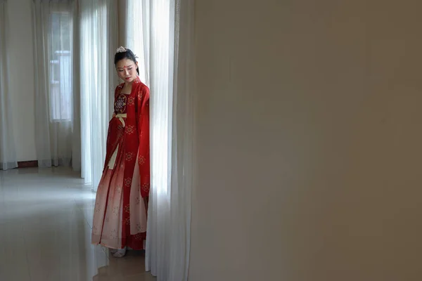 若い魅力的なアジアの女性を身に着けている伝統的な中国の赤い半布ロングスカートの衣装スカーフヘアピンピアス室内で窓の白いカーテンライト — ストック写真