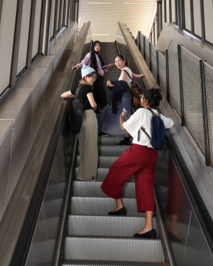 Dört grup genç, çekici, Asyalı, çok ırklı, çok ırklı kız arkadaş öğrenciler konuşuyor, geziyorlar, gezintiye çıkıyorlar, sırt çantalı, cep telefonlu not defterleri asansörde yükseliyor.