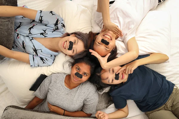 Young Asian girls sleepover pajama party blackhead remover nose patch on large bed in bedroom with bright light window fun happy joy funny laugh