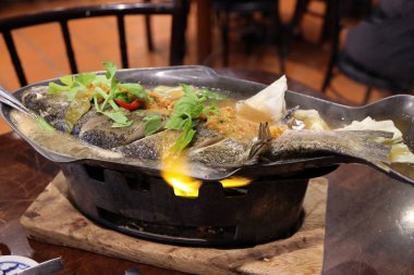 Tayland usulü sarımsaklı limon buharlı levrek balığı sıcak balık tabağında servis edilen ateş buharı. 