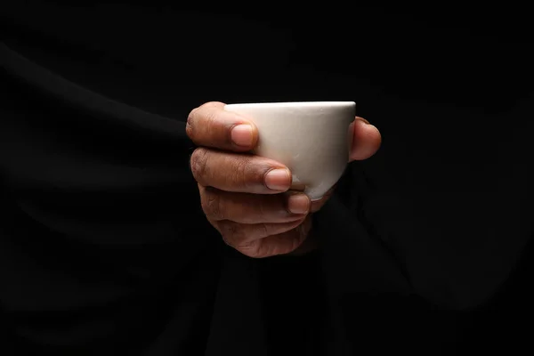Asian male dark skinned single hand fist finger on black background holding white Japanese Chinese teacup