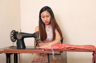 Genç Asyalı kadın, eski bir dikiş makinesinde terzi kumaşı kullanıyor. 