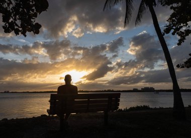 Yalnız bir adam bankta oturmuş güzel bir gün batımını seyrediyor. yumuşak odak