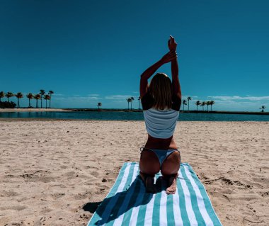 Bir kız ellerini okyanusta bir havluya koyup oturur. Yumuşak odak