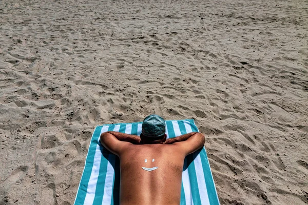 Facet Leży Brzuchu Ręczniku Plażowym Uśmiechnięta Twarz Jest Narysowana Śmietanką — Zdjęcie stockowe