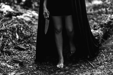 A girl in a dark robe with a knife. It stands in the forest. Happy Halloween. All Saints' Day. Black and white photo. Soft focus clipart