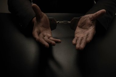 Siyah takım elbiseli bir işadamı, bir masaya ve siyah bir masaya kelepçelenmiş olarak, elini kaldırarak polisin serbest bırakılmasını anlatıyor. Yolsuzluk, rüşvet, yasadışı işlemler