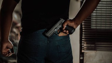 Arkasında silah olan siyah gömlekli bir hırsız soygunculuk yapmak için bir evin kapısını kırıyor..