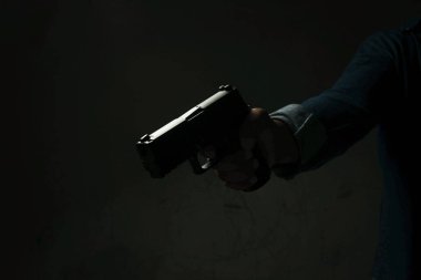 Mavi kot gömlekli bir adam elinde tabancayla karanlık bir odada duruyor. Nişan al ve silahı hedefe doğrult. Suikast, cinayet, suç kavramı