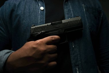 Mavi kot gömlekli bir adam karanlık bir odada duruyor ve göğsüne silah dayıyor. Suikast, cinayet, suç kavramı