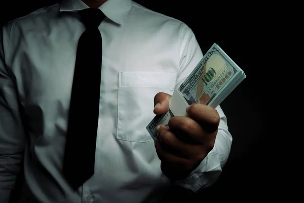 Siyah arka planda dolar tutan bir iş adamı. Metin girişi için yer var. yozlaşma, rüşvet.