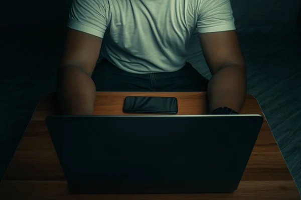 Beyaz gömlekli bir adam karanlık bir odada dizüstü bilgisayarın üzerinde oturuyor. Işık parlıyor. İnternet kavramı bağımlılığı.üst görünüm.