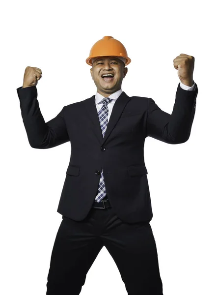 一位英俊的总工程师身穿黑色西服 头戴橙色头盔 双手紧握着拳头 非常快乐的样子 与白色背景隔离 有着剪路 — 图库照片