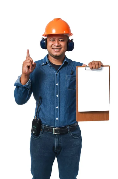 这位年轻的工程师戴着头盔和耳罩 穿着长袖衬衫和长裤 拿着剪贴板站着 在白色背景上与剪贴板隔离 复制空间 — 图库照片