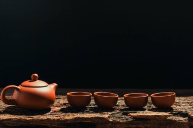 Sürahiler ve çay fincanları eski ahşap üzerine dizilmiş, siyah arka plan.