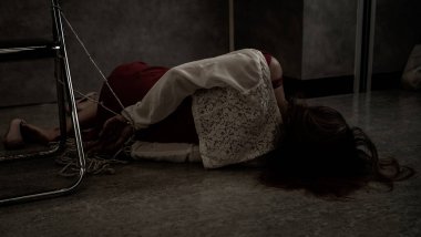 Kırmızı elbiseli bir kadın, gri ve siyah korkunç bir odada baygın bir şekilde sandalyeye bağlanır. Adam kaçırma, fuhuş, rehine. kopyalama alanı ile.