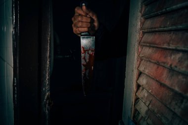 A male murderer holding a bloodstained knife that kills his victim in a very terrifying and terrifying way.