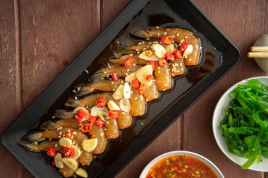 Soya sosu ya da shoyu sosunda salamura edilmiş karidesler acı biber ve baharatlı sosla dilimlenmiş sarımsak serpiştirilmiş deniz yosunu ve Japon pirinci kahverengi ahşap masadaki mezeler..