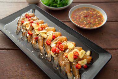 Soya sosu ya da shoyu sosunda salamura edilmiş karidesler acı biber ve baharatlı sosla dilimlenmiş sarımsak serpiştirilmiş deniz yosunu ve Japon pirinci kahverengi ahşap masadaki mezeler..