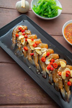 Soya sosu ya da shoyu sosunda salamura edilmiş karidesler acı biber ve baharatlı sosla dilimlenmiş sarımsak serpiştirilmiş deniz yosunu ve Japon pirinci kahverengi ahşap masadaki mezeler..