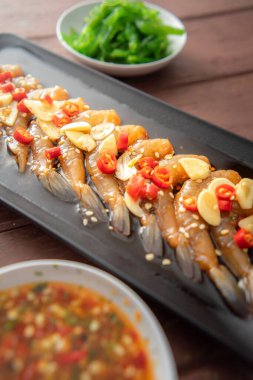 Soya sosu ya da shoyu sosunda salamura edilmiş karidesler acı biber ve baharatlı sosla dilimlenmiş sarımsak serpiştirilmiş deniz yosunu ve Japon pirinci kahverengi ahşap masadaki mezeler..