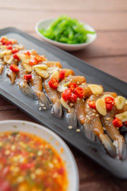 Soya sosu ya da shoyu sosunda salamura edilmiş karidesler acı biber ve baharatlı sosla dilimlenmiş sarımsak serpiştirilmiş deniz yosunu ve Japon pirinci kahverengi ahşap masadaki mezeler..