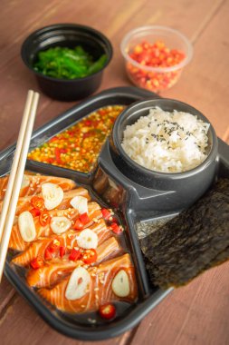 Soya soslu ya da Shoyu soslu somon salamurası ve üzerine kırmızı biber ve dilimlenmiş sarımsak serpiştirilmiş. Baharatlı soslu deniz yosunu ve Japon pilavı kahverengi ahşap bir masada yan yemeklerdir..