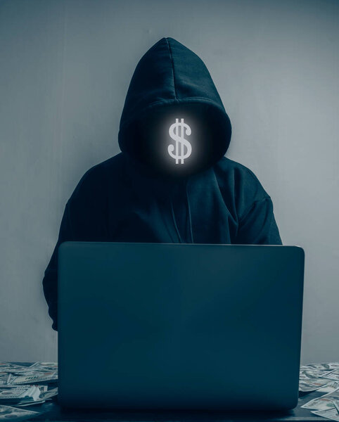 The hacker is wearing a black hoodie. They are stealing huge financial data on computers and have lots of dollars lying around.