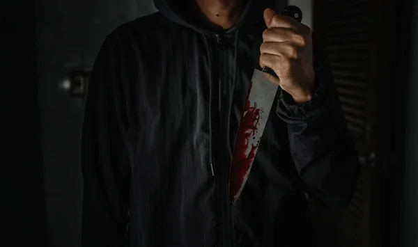 A male murderer holding a bloodstained knife that kills his victim in a very terrifying and terrifying way.
