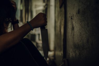 The shadow of a female murderer stood with a knife in a terrifying wasteland, illuminated from behind.Scary horror or thriller movie mood or nightmare at night Murder or homicide concept.