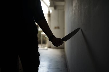 The shadow of a female murderer stood terrifyingly holding a knife and lit from behind.Scary horror or thriller movie mood or nightmare at night Murder or homicide concept.Focus on the knife.