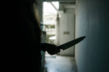 The shadow of a female murderer stood terrifyingly holding a knife and lit from behind.Scary horror or thriller movie mood or nightmare at night Murder or homicide concept.Focus on the knife.