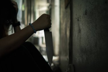 The shadow of a female murderer stood with a knife in a terrifying wasteland, illuminated from behind.Scary horror or thriller movie mood or nightmare at night Murder or homicide concept.Focus on the knife.
