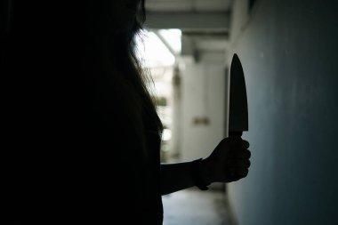 Kadın bir katilin gölgesi korkunç bir şekilde elinde bir bıçakla ve arkadan aydınlatılarak dikildi. Korku ya da gerilim filmi havası ya da gece vakti cinayet ya da cinayet kavramı. Bıçağa odaklan..