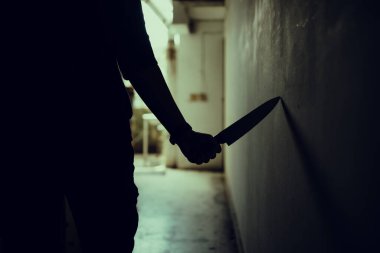 The shadow of a female murderer stood terrifyingly holding a knife and lit from behind.Scary horror or thriller movie mood or nightmare at night Murder or homicide concept.