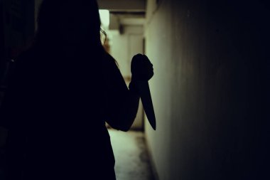 The shadow of a female murderer stood terrifyingly holding a knife and lit from behind.Scary horror or thriller movie mood or nightmare at night Murder or homicide concept.