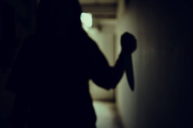 The shadow of a female murderer stood terrifyingly holding a knife and lit from behind.Scary horror or thriller movie mood or nightmare at night Murder or homicide concept.