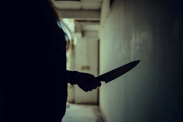 The shadow of a female murderer stood terrifyingly holding a knife and lit from behind.Scary horror or thriller movie mood or nightmare at night Murder or homicide concept.