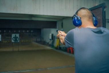 Kulaklık ve gözlük takan profesyonel bir adam atış poligonunda 9mm 'lik bir tabancayla pratik yapıyor..