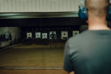 Kulaklık ve gözlük takan profesyonel bir adam atış poligonunda 9mm 'lik bir tabancayla pratik yapıyor..