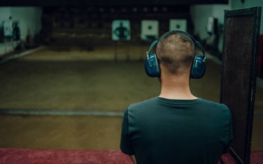 A professional man wearing earmuffs and goggles is practicing shooting a 9mm pistol inside a shooting range.