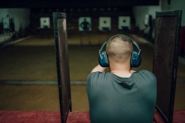 Kulaklık ve gözlük takan profesyonel bir adam atış poligonunda 9mm 'lik bir tabancayla pratik yapıyor..