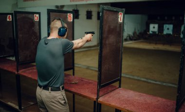 Kulaklık ve gözlük takan profesyonel bir adam atış poligonunda 9mm 'lik bir tabancayla pratik yapıyor..