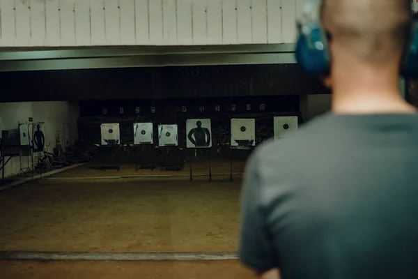 A professional man wearing earmuffs and goggles is practicing shooting a 9mm pistol inside a shooting range.