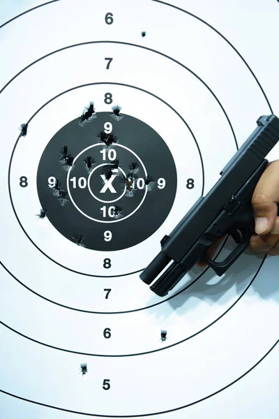 Man's hand holding a pistol on a shooting target with bullet holes. close-up
