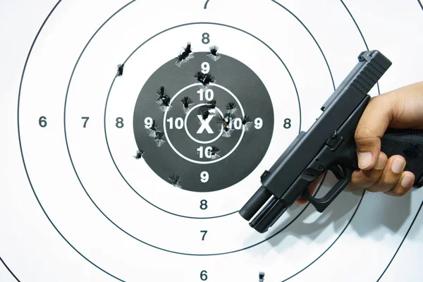 Man's hand holding a pistol on a shooting target with bullet holes. close-up
