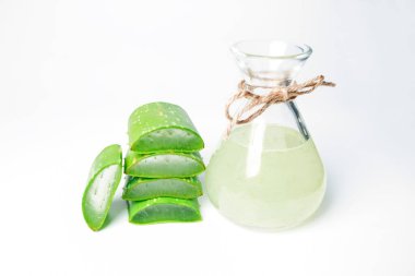 Taze aloe yaprakları dilimlenmiş ve beyaz bir arka planda cam bir kavanozda aloe suyu ile istiflenmiş. Yakın plan.
