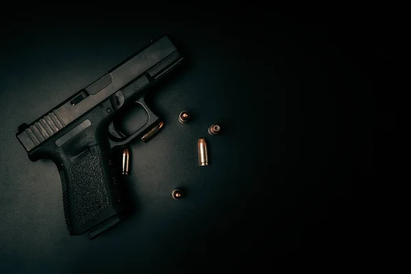 A black 9mm pistol on a black background with 9mm ammunition next to it. top view