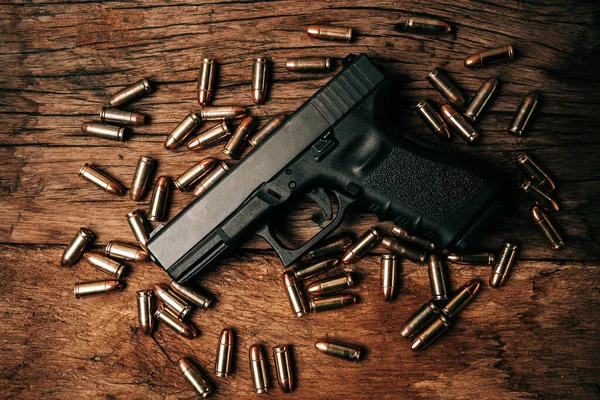 Portrait of a black 9mm pistol on an old wooden floor with 9mm ammunition next to it. top view