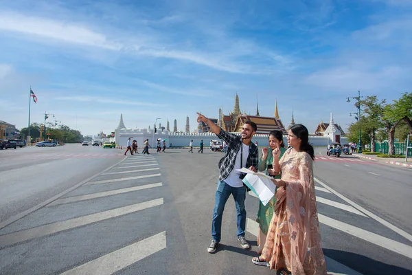 South Asian tourists backpackers looking a map for direction while traveling around traveling on holidays tourist landmark behind Wat Phra Kaew or Emerald Buddha Temple Bangkok Thailand.